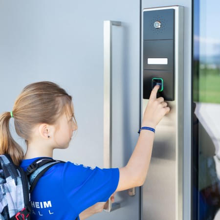 Ein Kind mit Schultasche öffnet die Haustür mit Fingerprint