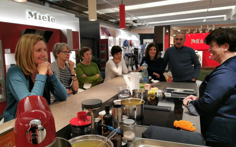 Eine Gruppe von Leuten hört der Vorführköchin zu.